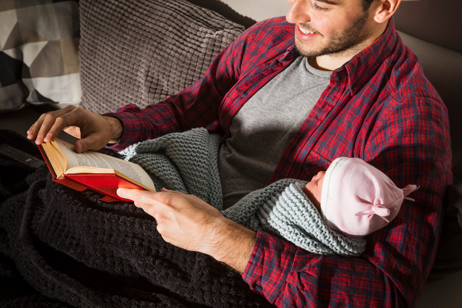 Father reading a parenting book while holding a newborn baby.